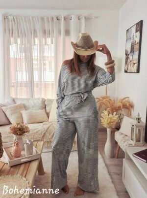 Une femme porte une combinaison rayée noir et blanche très confortable pour la mi saison décolletée avec ceinture, évasée dans le bas