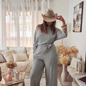 Une femme porte une combinaison rayée noir et blanche très confortable pour la mi saison décolletée avec ceinture, évasée dans le bas